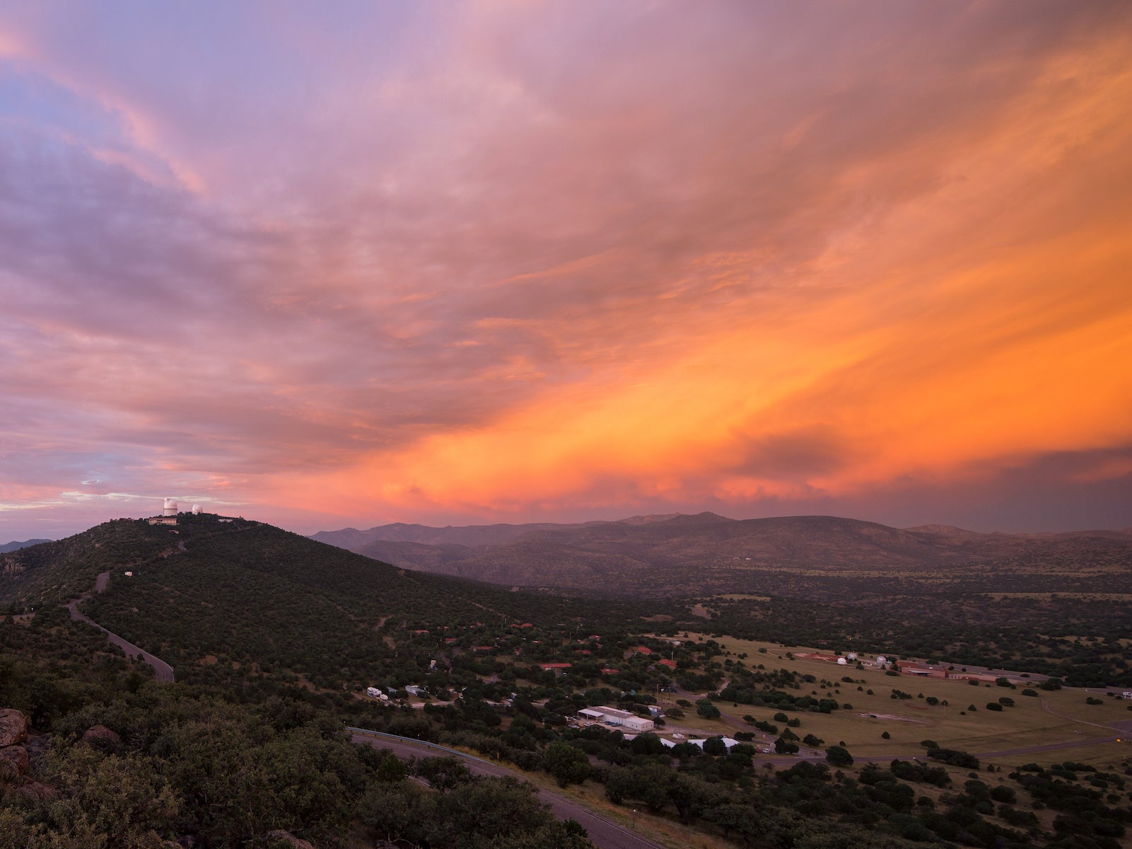 Sunrise over mountains covered in trees with buildings and an observatory in the foregroud